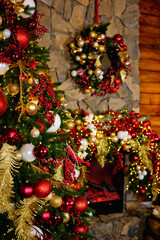 Selective focus. Decorated Christmas tree. Red and gold balls and lighted garland with lanterns. Christmas trinkets on the background of a stone fireplace. Decoration of the winter holiday with light