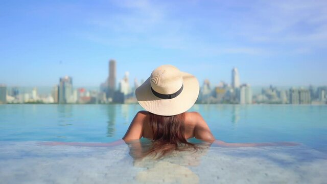 Back View of Stylish Woman in Infinity Rooftop Pool With Stunning View of Modern Cityscape in Background