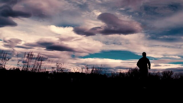 Beautiful black silhouette outline of a male jogger, jogging against a dramatic sky.  The jogger runs away from the camera from left to right.  A wide angle frames this stunning clouds and scenery.