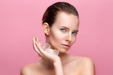 Beautiful caucasian young woman with perfect skin holds ice cube near face on pink studio background