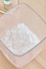 Detailed shot of a box of ice cubes. The box has a square shape. The plastic item is standing on the wooden table. There is glass on the background.