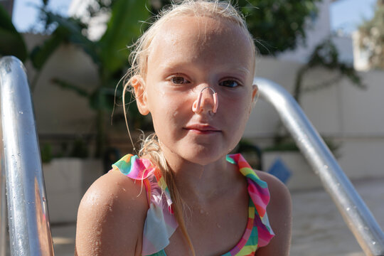 Close up portrait of wet blond preschool girl wearing nose clip for swimming. Girl is sitting near the pool outdoors on a summer day. Kid's sport concept