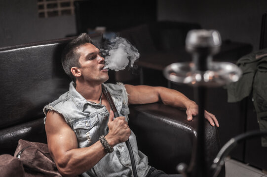 Sexy guy exhales smoke in hookah cafe.