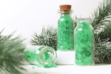 Bottles of sea salt on podium and fir branches for aromatherapy and spa on white table background