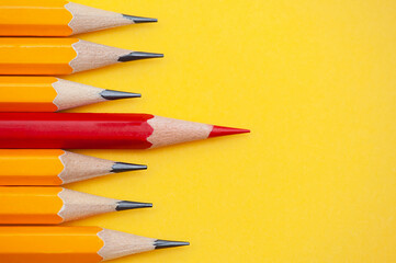 The red pencil stands out from the group of other pencils on the yellow background. Leadership, independence, uniqueness, initiative, strategy.