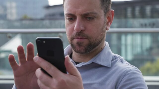 Close up of serious middle-aged beard man holding a cellphone typing to send a message in balcony businessman using mobile phone in people lifestyles with mobile technology