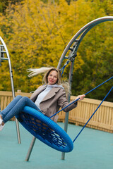 Young smiling blonde woman with braces swinging on the swing on playground and smiling