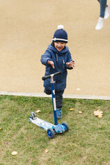 Cute baby boy riding on a scooter in autumn park in stylish casual outfit