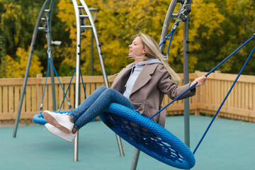 Young smiling blonde woman with braces swinging on the swing on playground and smiling