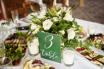 Beautiful floral arrangement of white rose flowers and greenery on wedding table in restaurant, copy space. Luxury wedding decorations. Table setting