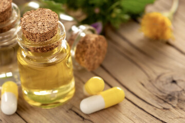 Essential oil or oil for natural diseases treatment in glass bottle on wooden table with capsules. Natural herbal medicine concept