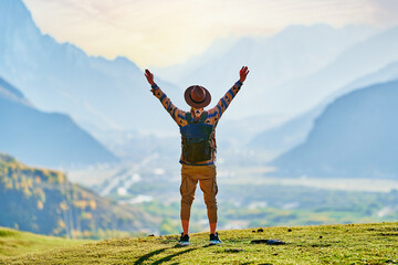 Hipster man traveler wanderer with open arms wearing hat and backpack standing alone and enjoying freedom and calm inspired travelling