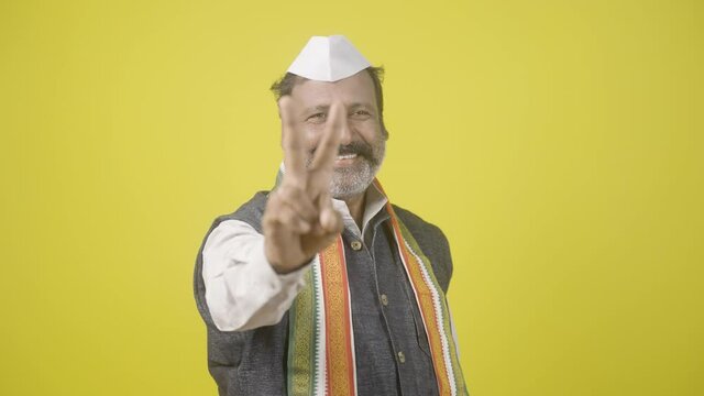 Slow motion shot of Happy Winner Politician celebrating while showing vitory sign in hand gesture by looking camera on Yellow Background - concept of Happiness, positive emotion, successful politician