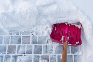 The view from the eyes of a person cleaning a thick layer of snow on a paving slab. There is a red...