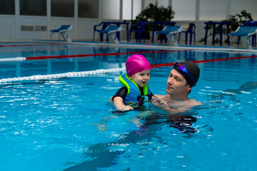 Happy father enjoying teaching his young daughter how to swim in swimming pool. Swimming lesson in...