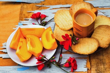 Kaki fruit, butter cookie, cup of coffee and red flower on scratched wooden table. - 472776901