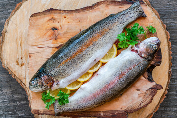 Two fresh raw rainbow trouts garnished with lemon slices and parsely