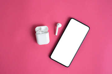 White wireless bluetooth headset , plastic case or box for storage and charging and smartphone on pink background, close-up