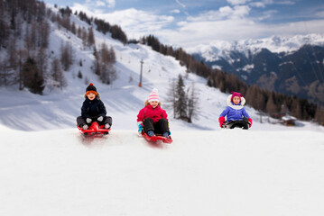 childhood, sledging and season concept - group of happy little kids sliding on sleds down snow hill...