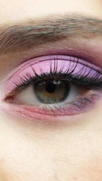 Closeup macro vertical video of human female eye with pink shadows.