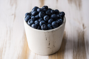 Blueberries in white ceramic bowl on rustic wooden background. Selective focus. Shallow depth of field.
