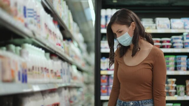 A girl goes to the refrigerator in a supermarket in a protective mask. Buy products in a mask