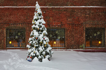 Snow covered Christmas tree. Outdoors with a decorated Christmas tree on a old red brick wall...