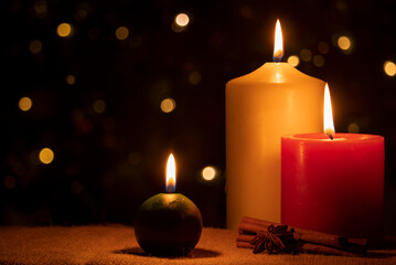 Burning Christmas candles with cinnamon and star anise on a dark background