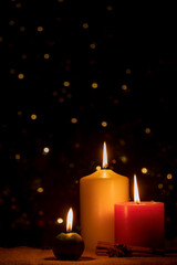 Burning Christmas candles with cinnamon and star anise on a dark background