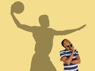Young man's dreams about big sport future. Conceptual image with man and shadow of strong male basketball player on yellow wall