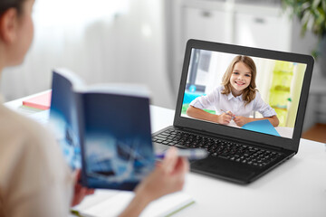 Fototapeta na wymiar distant education, school and people concept - female math teacher with smiling student girl on laptop computer screen and book having online class at home