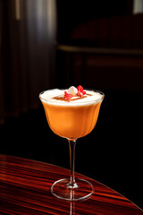 A cocktail with foam in a beautiful coupe glass garnished with edible flowers, big ice cube