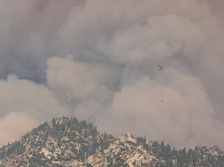 Fire helicopter with water bucket flying into smoke and fire clouds from wildfire at Black Mountain, Southern Sierra Nevada Mountains, California, from drought stressed forest