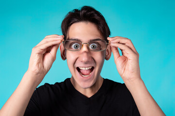 A funny man with glasses makes grimaces at the camera. Portrait of a guy against a blue background.