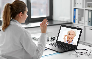 Fototapeta na wymiar healthcare, technology and medicine concept - female doctor with laptop computer having video call with senior patient at hospital