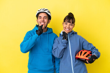 Young cyclist couple isolated on yellow background smiling with a sweet expression