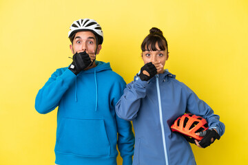 Obraz premium Young cyclist couple isolated on yellow background covering mouth with hands for saying something inappropriate