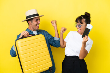 Young traveler friends holding a suitcase and passport isolated on yellow background celebrating a...