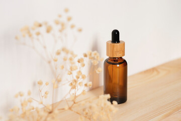 Amber dropper bottle with serum or essential oil on natural wooden background with daylight. Skincare products , natural cosmetic with with dry plants. Beauty concept for face body care
