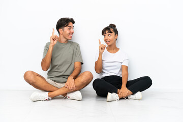 Fototapeta na wymiar Young mixed race couple sitting on the floor isolated on white background unhappy and frustrated with something