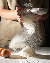 In the hands of a sieve with flour, which is poured onto the table where the eggs lie