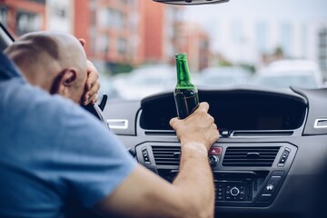 Man drives a car with a bottle of beer behind the wheel of a car. Dangerous situation on road.