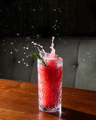Red cocktail with sprig of rosemary in highball with splash stands on wooden table