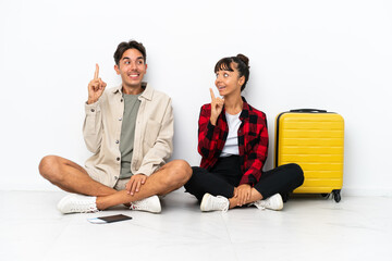Fototapeta premium Young mixed race travelers couple sitting on the floor isolated on white background intending to realizes the solution while lifting a finger up