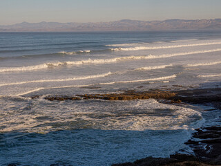 Obraz premium Pacific Ocean at Morro Bay, California, Montana de Oro State Park in foreground, Morro Rock in background, just before sunrise