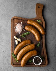 Grilled sausages on wooden board with garlic, rosemary and sea salt on gray background
