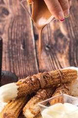 Hot churros with chocolate sauce on wooden table.
