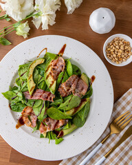 Salad with bacon, spinach, avocado and pine nuts in a white plate on the table