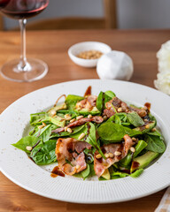 Salad with bacon, spinach, avocado and pine nuts in a white plate on the table