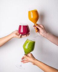 Three glasses of smoothies (orange, red and green) in hands on a white background